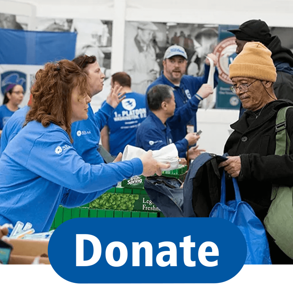 A large blue button reads Donate over an image of volunteers in blue long-sleeve shirts working a donation line where a woman greets an asian man opening his backpack.
