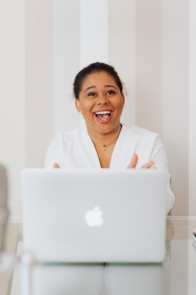 Elated by email marketing services, a woman using a laptop beams behind a laptop in a modern office desk indoors.
