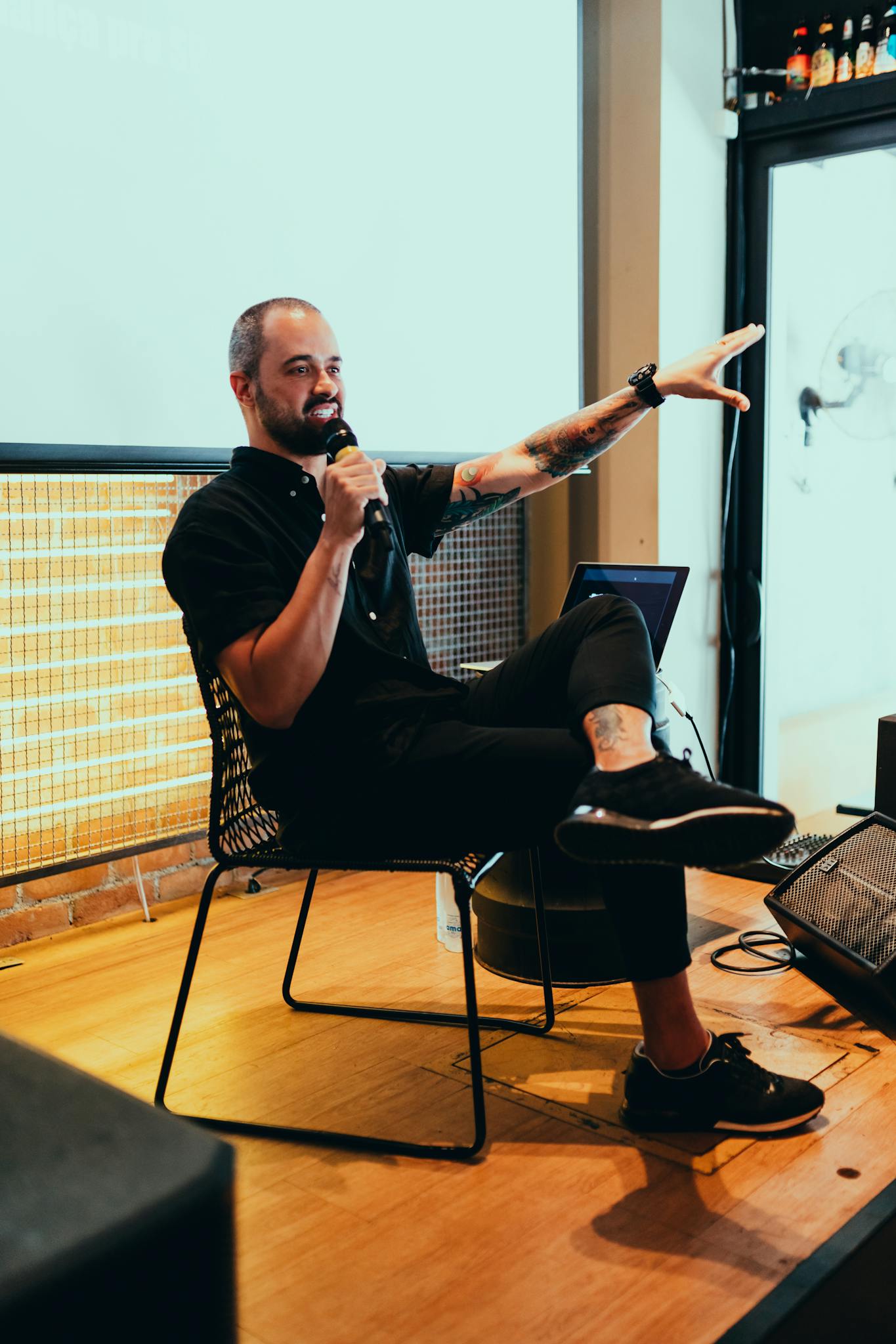 A bald man enthusiastically speaks through a microphone with his arm extended during a presentation with a boutique marketing agency.