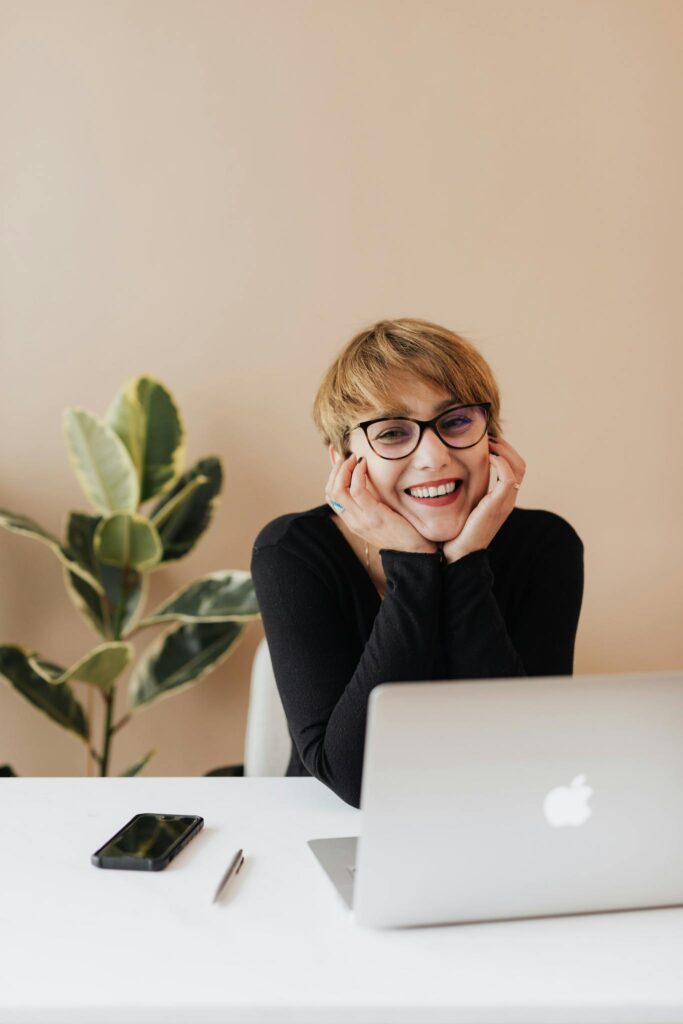 A woman smiles at her desk with a content marketing Mac book on her desk and a plant in the background.